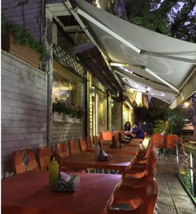 فضای باز دلپذیر فست فود یوریک در شب، با ردیفی از میز و صندلی‌های نارنجی و سایبان‌های مدرن برای راحتی مشتریان.