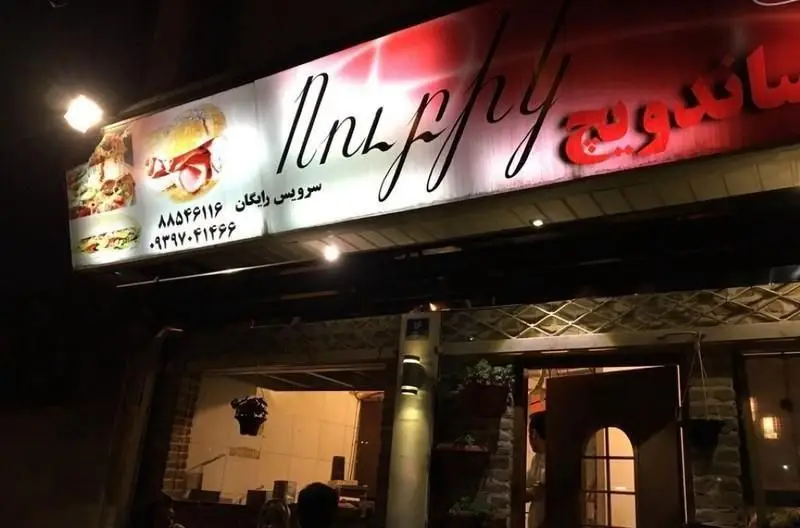 تابلوی نورانی فست فود یوریک در شب با عکس ساندویچ و پیتزا، سرویس رایگان و شماره تماس‌ها. ورودی رستوران یوریک نیز دیده می‌شود.