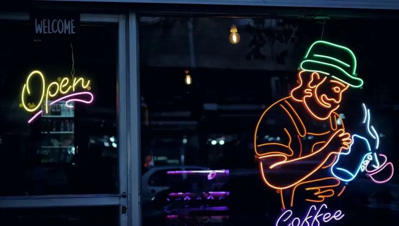 ورودی کافه امیر با تابلو نئون روشن باریستا، کلمه Open و Welcome. فضایی دلنشین برای علاقه‌مندان به قهوه.