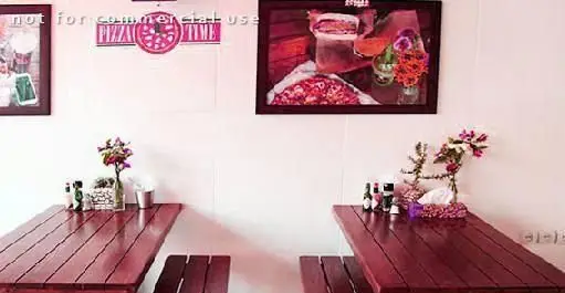 فضای داخلی رستوران فست فود آوان با میزهای چوبی و دکوراسیون جذاب. تصاویری از پیتزا و ساعت پیتزا روی دیوارها. محیطی عالی برای غذا.