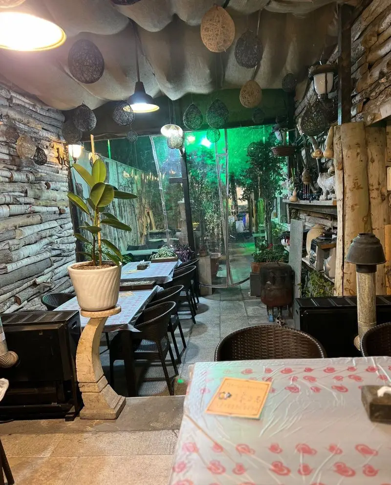 محیط دنج و آرام ماهی سرا شب های ریحان با دیوارهای چوبی و سقف تزئینی، همراه با چشم انداز فضای سبز دلنشین برای مشتریان.