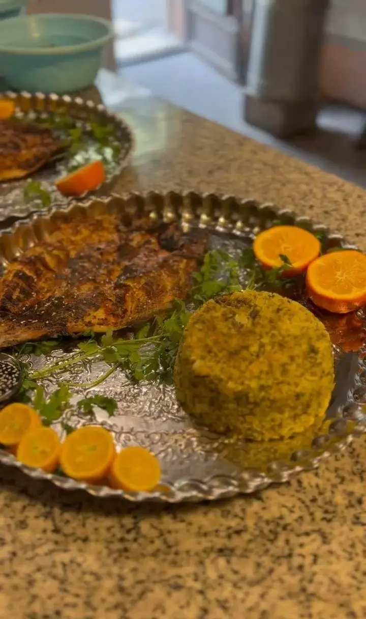 سرو ماهی کباب طلایی و پلو سبزی معطر روی سینی نقره‌ای در ماهی سرا شب های ریحان، همراه با مرکبات و سبزی تازه، تجربه‌ای دلنشین.