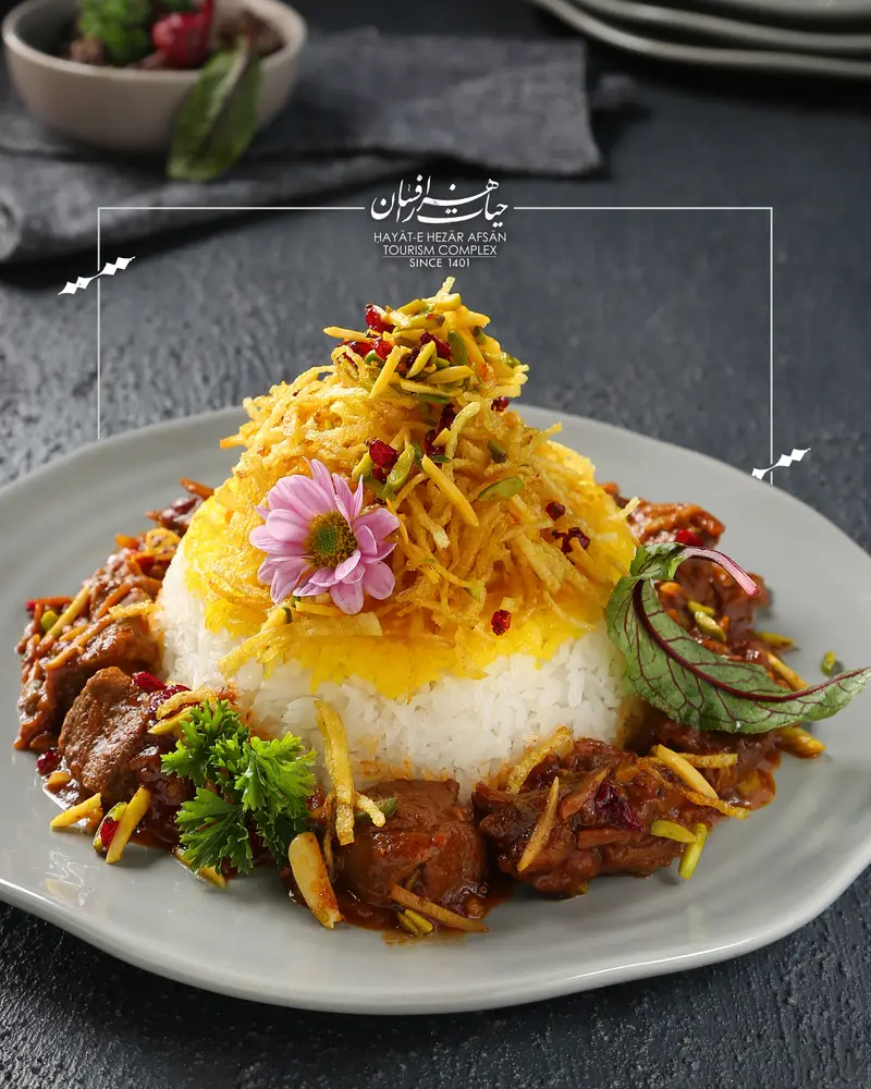غذای سنتی و دلنشین ایرانی کافه حیات هزار افسان: پلو زعفرانی با خلال سیب زمینی و خورش گوشت و بادام، تزیین گل.