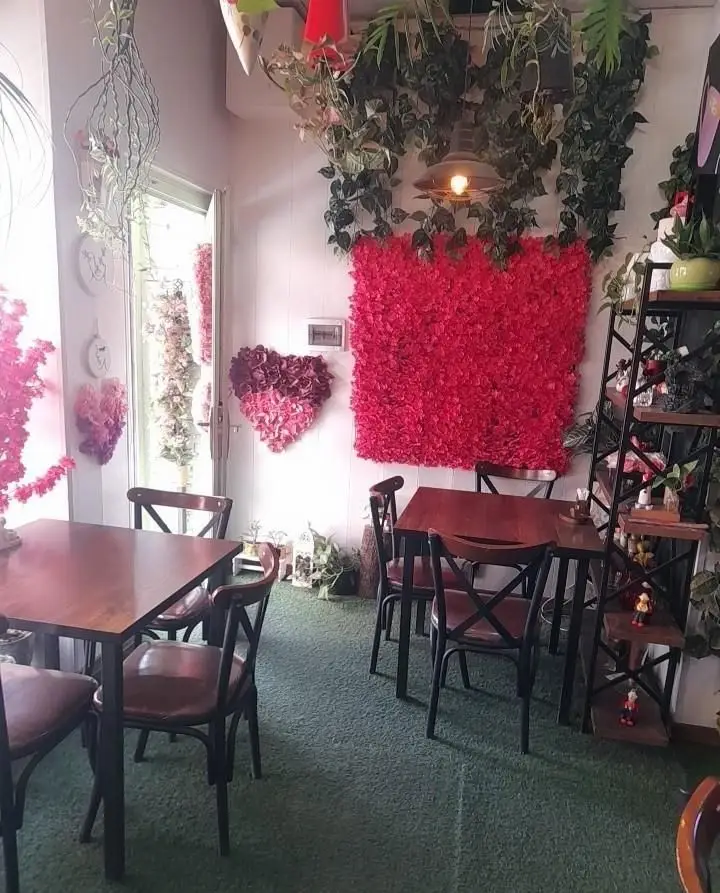 دکوراسیون شیک و گل‌آرایی‌شده کافه دونه نارمک با دیوار گل قرمز، قلب‌های رمانتیک، گیاهان آویز و مبلمان راحت. فضایی دنج برای مشتریان.