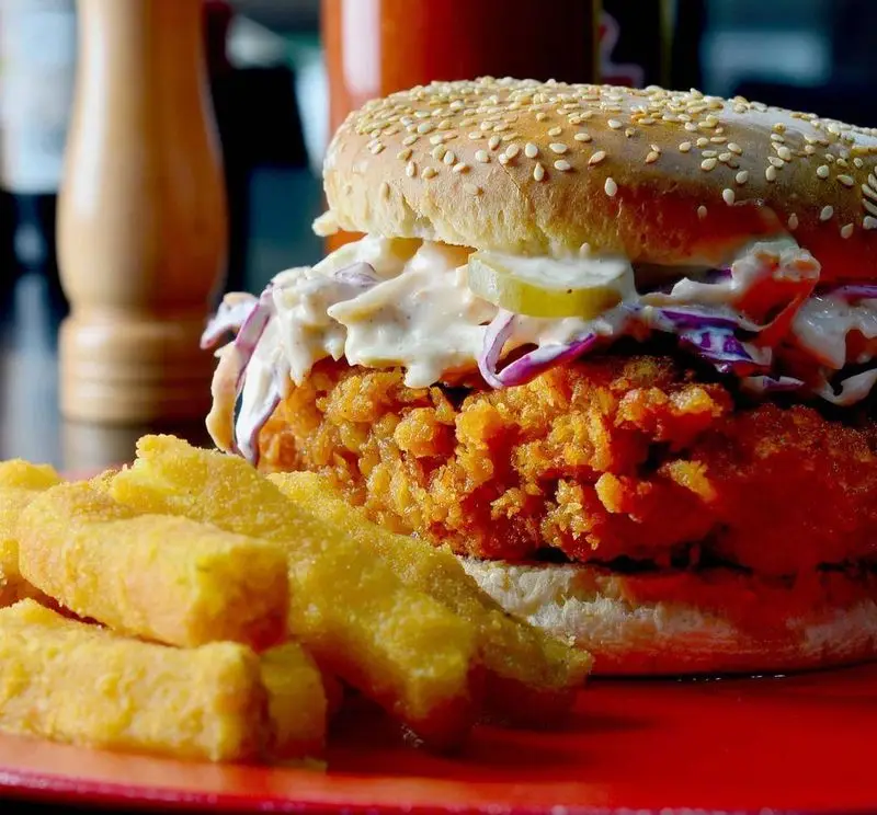 ساندویچ مرغ سوخاری طلایی و خوشمزه فست فود پاندا با کول اسلو خامه‌ای، ترشی و نان کنجدی، سرو شده با سیب زمینی سرخ کرده.