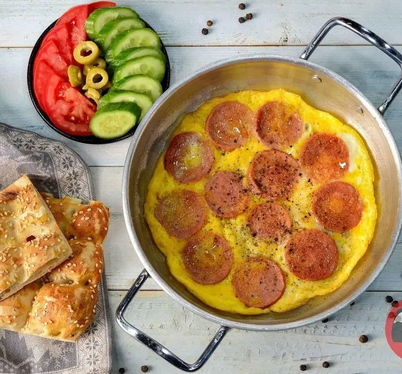 صبحانه لذیذ و پرانرژی از فست فود پاندا: املت با کالباس داغ در تابه، نان کنجدی، گوجه، خیار و زیتون. بهترین گزینه برای شروع روز!