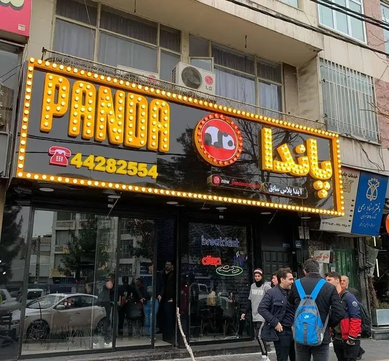عکس تابلوی روشن و زیبای فست فود پاندا به زبان انگلیسی و فارسی، همراه با لوگوی جذاب پاندا، شماره تلفن 44282554 و ورودی شلوغ رستوران.