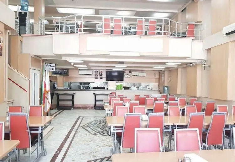 سالن داخلی رستوران جوان هنرور ۱ با میز و صندلی‌های متعدد، فضای طبقه بالا، کانتر آشپزخانه و محیطی تمیز برای پذیرایی از مشتریان.