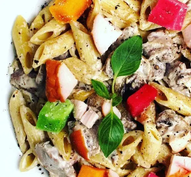 نمای نزدیک پاستا پنه غلیظ و لذیذ با سس خامه ای قارچ، تکه های مرغ، فلفل دلمه رنگی و برگ ریحان تازه از پاستا چنگال.