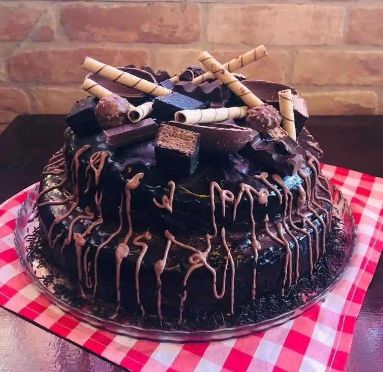 کیک شکلاتی جذاب و خوشمزه کافه اوتن؛ یک کیک دو طبقه با گاناش تیره، سس شکلات قطره‌ای و تزئینات ویفر، ترافل و تکه‌های شکلات.