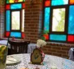 فضای داخلی دنج و زیبای کافه رستوران عمارت نیلی با دیوارهای آجری و پنجره‌های رنگی سنتی، مکانی آرام برای استراحت و غذا.