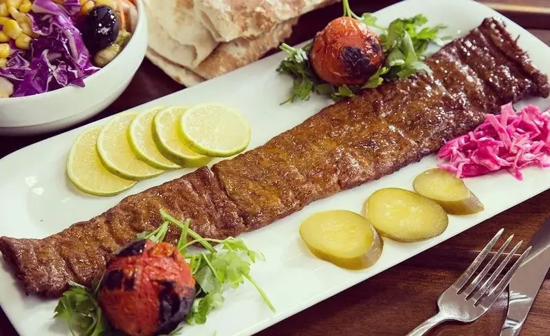 کباب کوبیده لذیذ باغچه رستوران سنتی صحرا، تزئین شده با لیمو، گوجه کبابی، ترشی و کلم قرمز، در کنار سالاد تازه.