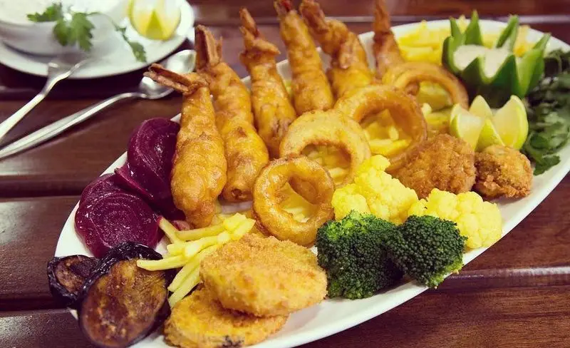 سینی میگو سوخاری و مرغ سوخاری در باغچه رستوران سنتی صحرا، همراه با سیب زمینی، پیاز حلقه ای و سبزیجات تازه.