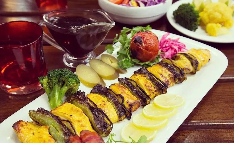 کباب مرغ و بادمجان باغچه رستوران سنتی صحرا با دورچین تازه لیمو، بروکلی، گوجه کبابی و سس رب انار. غذای خوشمزه ایرانی.