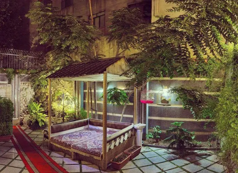 باغچه رستوران سنتی صحرا: فضای دنج شبانه با تخت سنتی ایرانی، فرش، نورپردازی گرم، درختان سرسبز و مسیر ورودی قرمز. محیطی آرام و دلنشین برای پذیرایی.