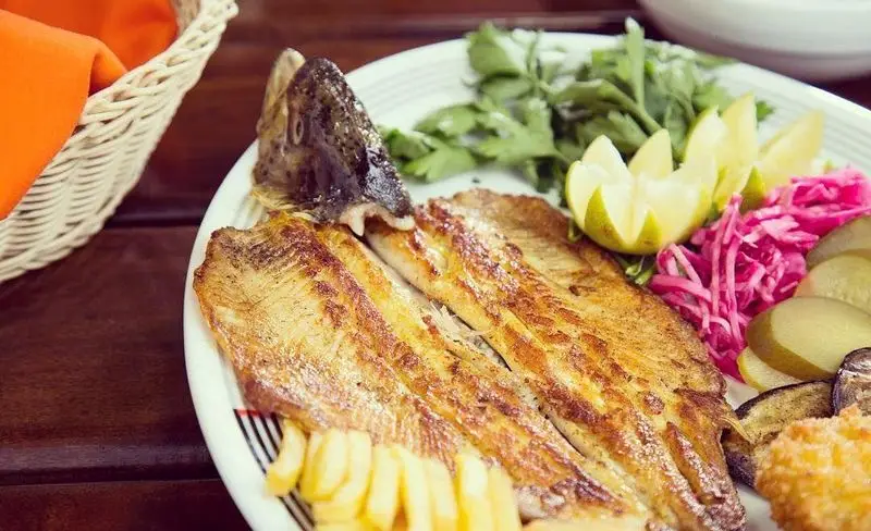 ماهی کبابی اصیل همراه با برش‌های لیمو، سبزیجات معطر، کلم ترش و سیب‌زمینی سرخ‌کرده در باغچه رستوران سنتی صحرا. لذت طعم تازه