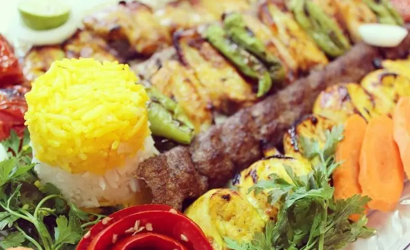 سفره رنگین و لذیذ کباب کوبیده و جوجه به همراه برنج زعفرانی، فلفل کبابی و سبزیجات تازه در باغچه رستوران سنتی صحرا
