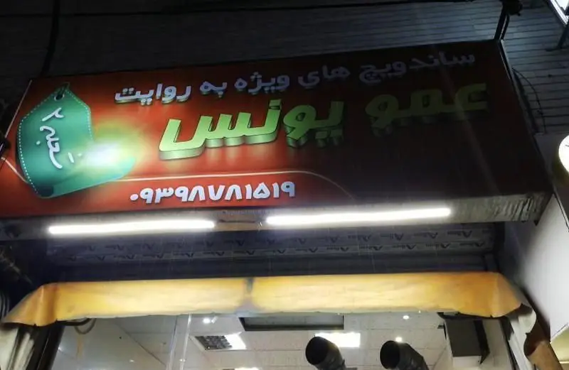 تابلو ساندویچی عمو یونس: ارائه دهنده ساندویچ‌های ویژه. حاوی شماره تماس ۰۹۳۹۸۷۸۱۵۱۹ و اشاره به شعبه ۲. بهترین گزینه برای غذای سریع و خوشمزه.