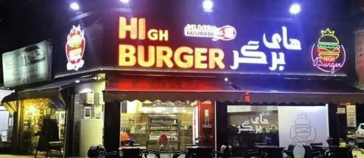 فست فود های برگر: نمای شبانه مغازه با تابلوهای نئونی درخشان نام رستوران، لوگوهای همبرگر آتشین و تاجی و شماره تماس سفارش.