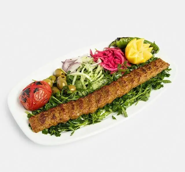 یک سیخ کباب کوبیده لذیذ از رستوران سنتی آفاق همراه با گوجه کبابی، زیتون، فلفل کبابی و سبزیجات تازه و دورچین.