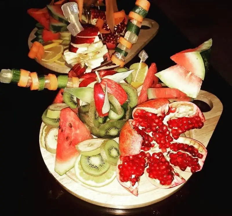 میوه آرایی مجلل و سینی‌های پربار میوه تازه در رستوران مروارید؛ شامل انار، کیوی، هندوانه، سیب. ایده‌آل برای پذیرایی و دسر.