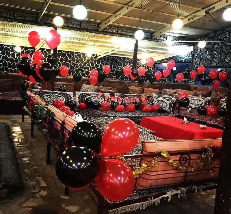 رستوران مروارید با دکوراسیون جشن تولد یا مناسبت عاشقانه، مزین به بالن‌های قرمز و مشکی و فضایی سنتی و آرامش‌بخش.
