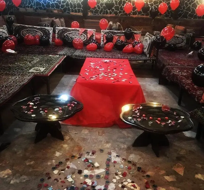 دکوراسیون رمانتیک و خاص رستوران مروارید برای مناسبت‌های ویژه با بادکنک‌های قرمز و مشکی، میز آرایی زیبا با گلبرگ و شمع.