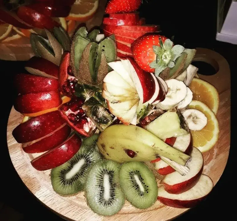 رستوران مروارید: بشقاب میوه لوکس و متنوع شامل سیب قرمز، توت فرنگی، کیوی، موز، پرتقال و انار، ایده‌آل برای دسر و سلامتی.