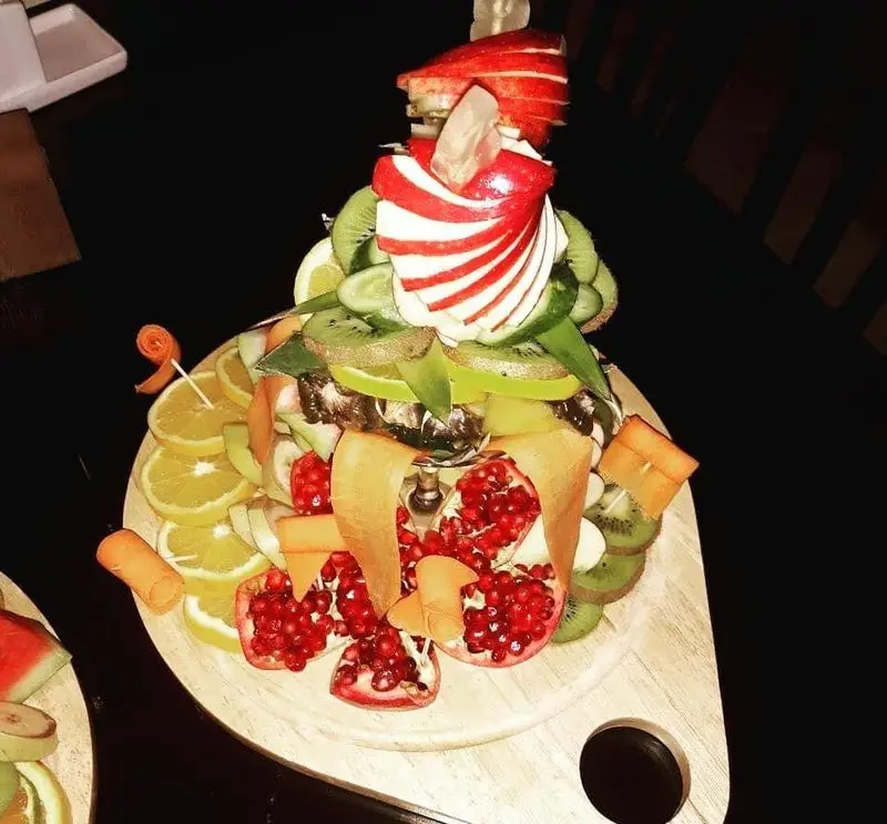 سینی میوه آرایی مجلل رستوران مروارید با میوه‌های تازه و رنگارنگ شامل سیب قرمز، کیوی سبز، پرتقال و دانه‌های انار، تزئینی زیبا و مناسب پذیرایی.