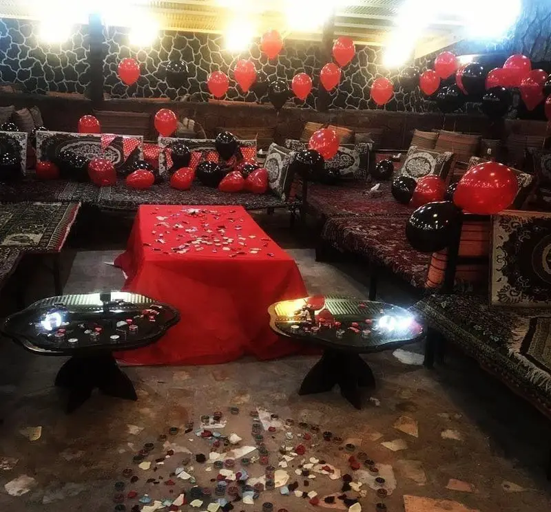 فضای رمانتیک رستوران مروارید با بادکنک‌های قرمز و مشکی، گلبرگ‌های رز روی میز و چیدمان سنتی دلنشین برای مناسبت‌های خاص.