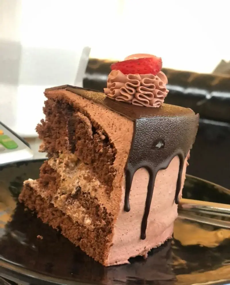 کیک شکلاتی اشتهابرانگیز با لایه‌های کرم کاکائویی و تزیین توت فرنگی و گاناش، دسری دلپذیر از کافه رستوران حیات نو.
