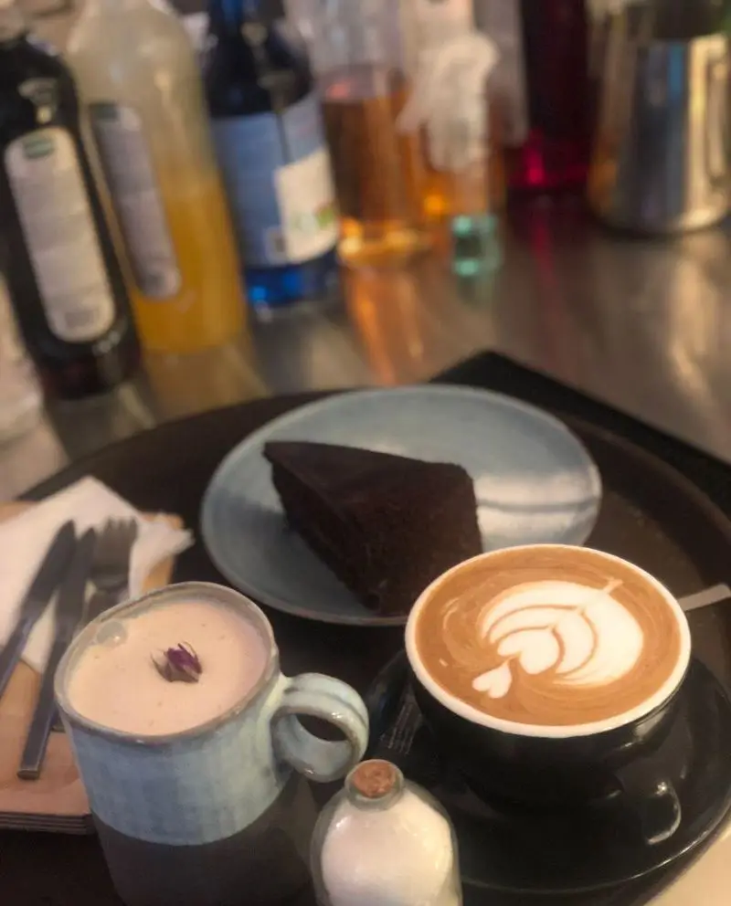 لذت نوشیدن قهوه لاته با لاته آرت هنرمندانه، در کنار دمنوش آرامش‌بخش و کیک شکلاتی خوشمزه در کافه رستوران حیات نو.