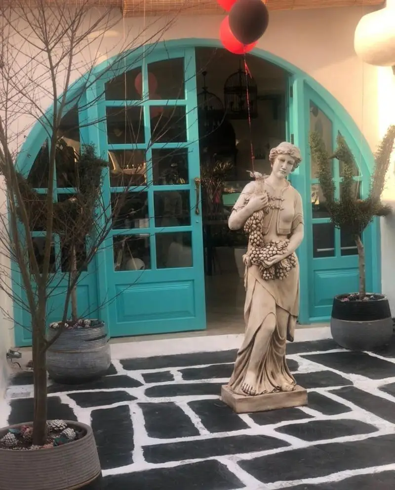 کافه رستوران حیات نو: فضای بیرونی دلنشین با درب ورودی آبی رنگ، مجسمه زن، و سنگفرش سیاه و سفید. مناسب تجربه ای خاص.