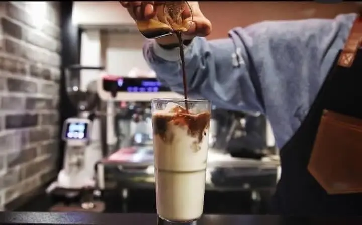 باریستا کافه رستوران حیات نو در حال تهیه آیس لاته تازه و دلچسب با ریختن اسپرسو در لیوان شیر. تجربه نوشیدنی خنک و خاص.