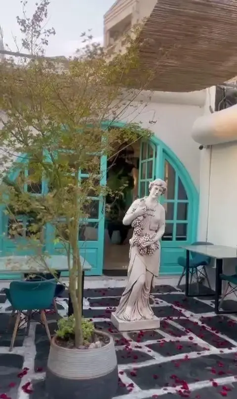 فضای زیبای کافه رستوران حیات نو با دکوراسیون مدیترانه‌ای، درب‌های فیروزه‌ای، مجسمه کلاسیک و گلبرگ‌های رز روی زمین.