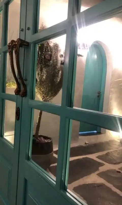 تصویری از ورودی زیبای کافه رستوران حیات نو با درب شیشه‌ای آبی فیروزه‌ای، راهروی سنگفرش و طراحی دلنشین فضای باز، شبیه به سبک سانتورینی.