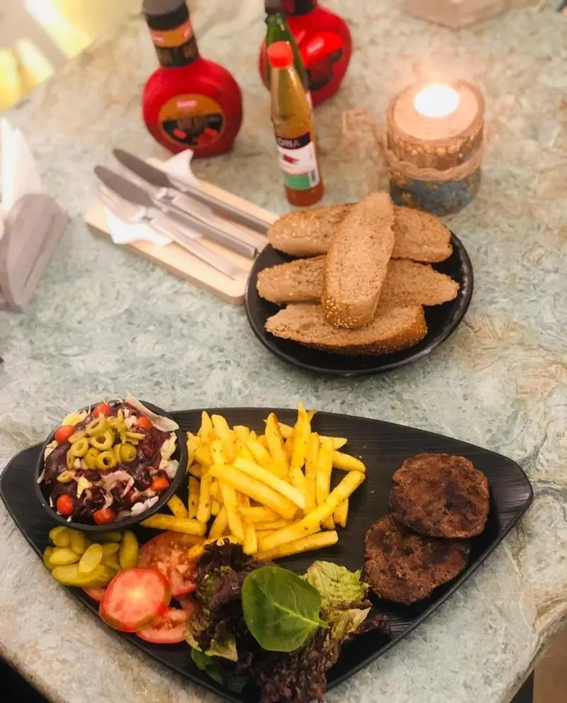 غذای خوشمزه کافه رستوران حیات نو شامل همبرگر، سیب زمینی سرخ کرده، سالاد و نان تازه در محیطی دلنشین و با شمع روشن.