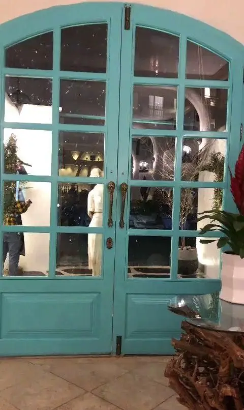 ورودی جذاب کافه رستوران حیات نو با درب دوجداره فیروزه‌ای شیشه‌ای، دستگیره‌های برنزی و نمایش‌دهنده فضای داخلی دلنشین و مدرن.