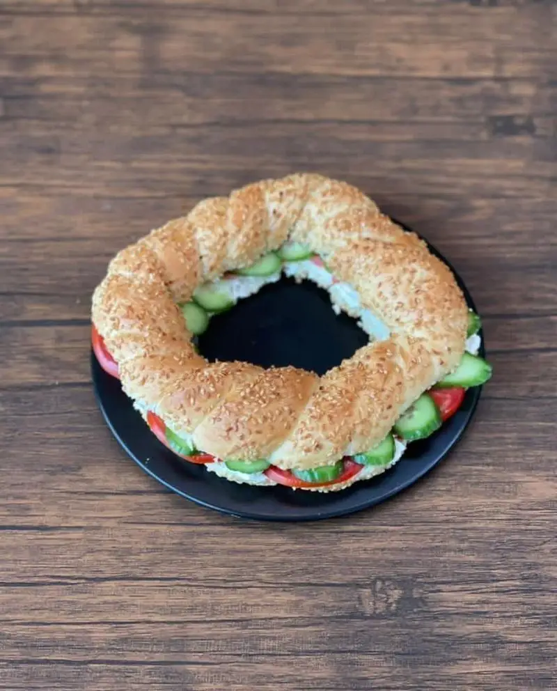 ساندویچ بزرگ سیمیت کنجدی پر شده با پنیر، خیار و گوجه فرنگی تازه، یک غذای خوشمزه از کافه رستوران حیات نو.