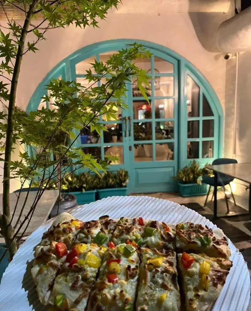 پیتزای سبزیجات با پنیر فراوان در فضای دلنشین کافه رستوران حیات نو با درب ورودی فیروزه‌ای. محیطی زیبا برای لذت بردن از غذای خوشمزه.