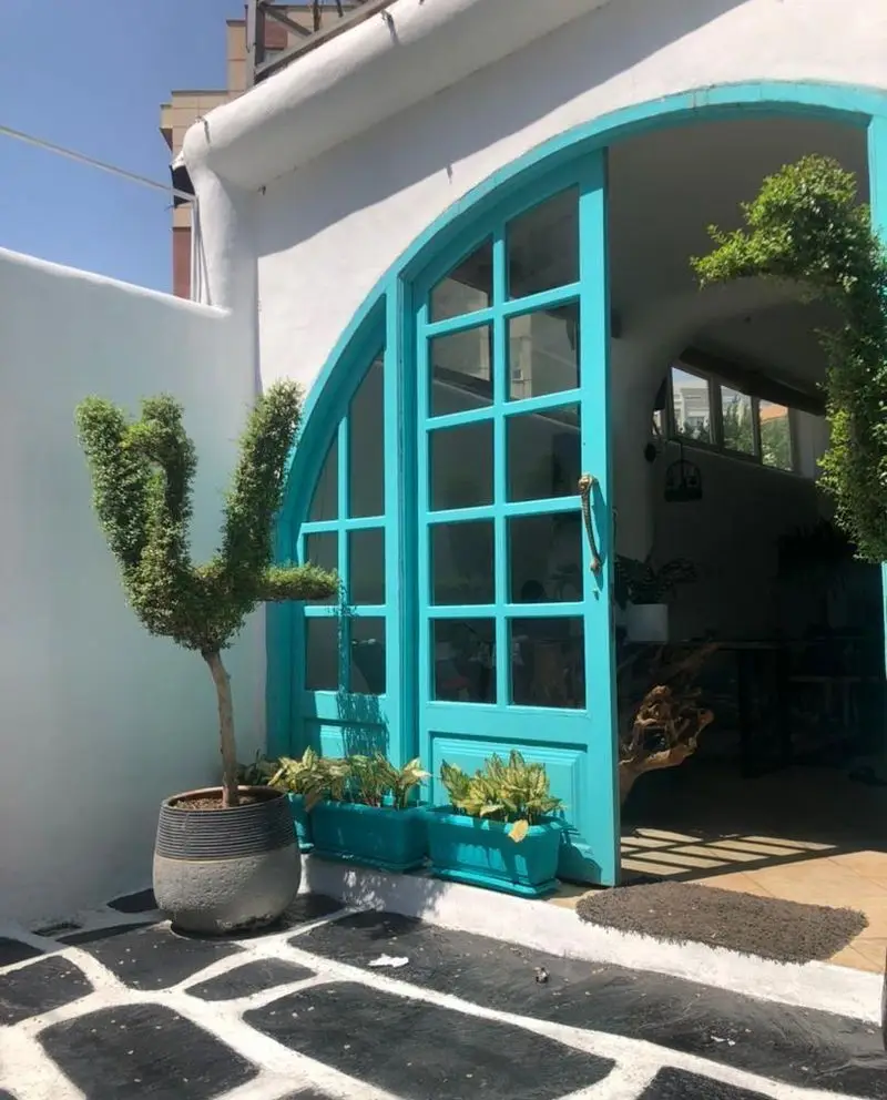 ورودی جذاب کافه رستوران حیات نو: در فیروزه ای قوسی، گلدان های زیبا و کفپوش سنگی سیاه و سفید، فضایی دلنشین و آفتابی برای آرامش.