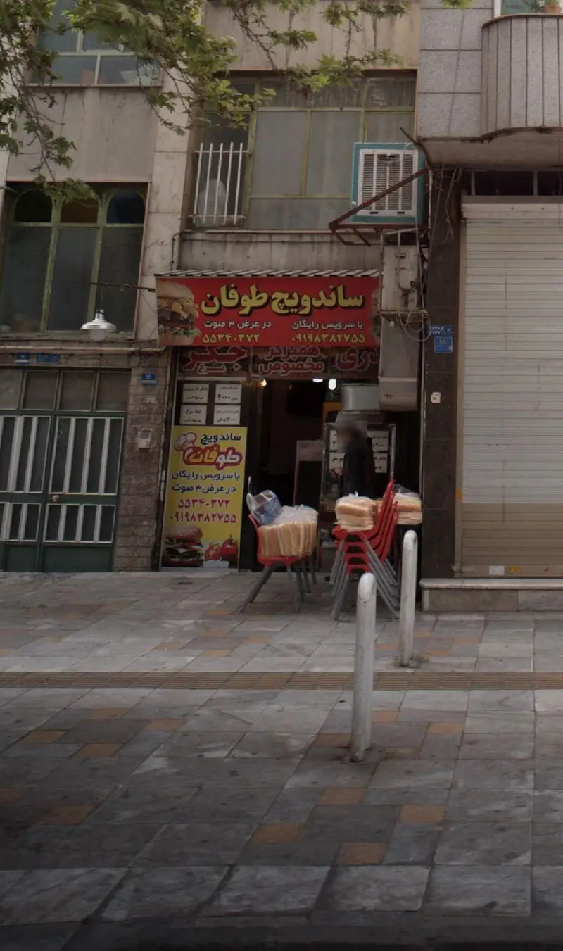 تصویر مغازه ساندویچ طوفان با تابلوی قرمز رنگ، عرضه ساندویچ و همبرگر مک مخصوص، همراه با شماره تماس و تحویل رایگان.