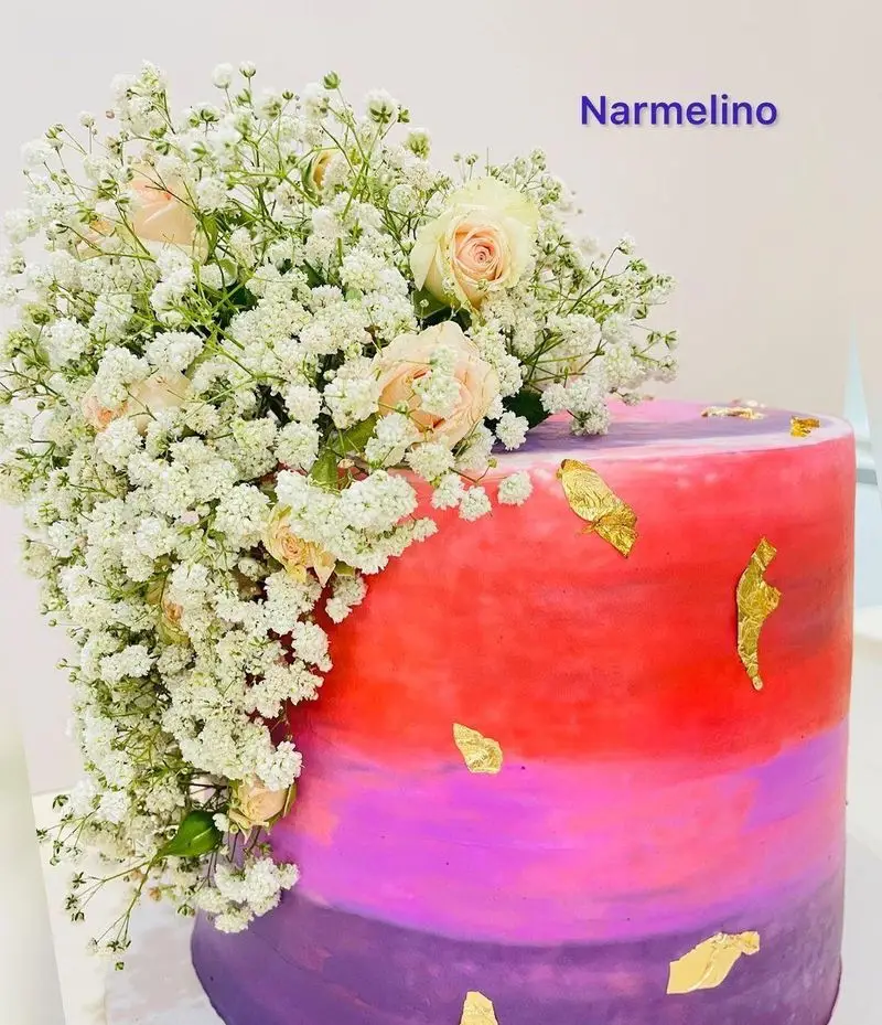 کیک لاکچری و زیبای قنادی نارملینو با دیزاین آمبره بنفش تا قرمز، تزیین خاص گل‌های عروس و رز صورتی با ورق طلا.
