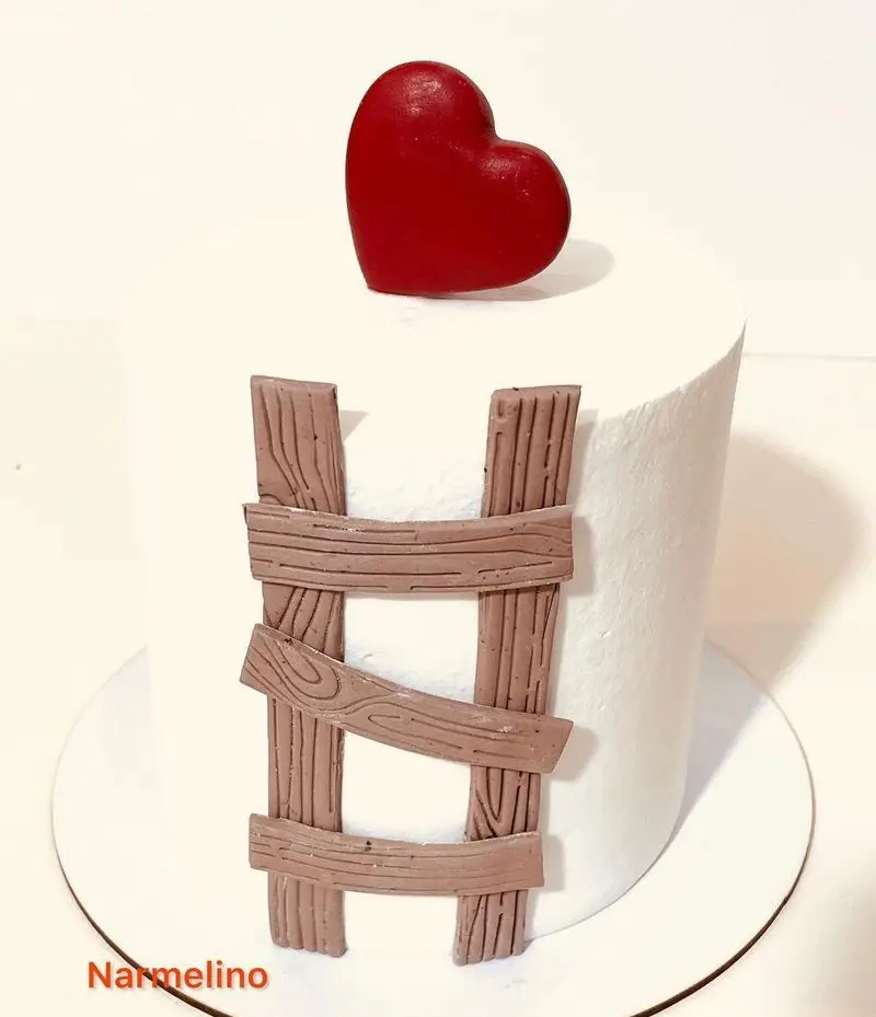 کیک سفید مینیمال قنادی نارملینو با تاپر قلب قرمز جذاب و تزئین نردبان چوبی دست‌ساز. کیکی خاص برای عزیزان.