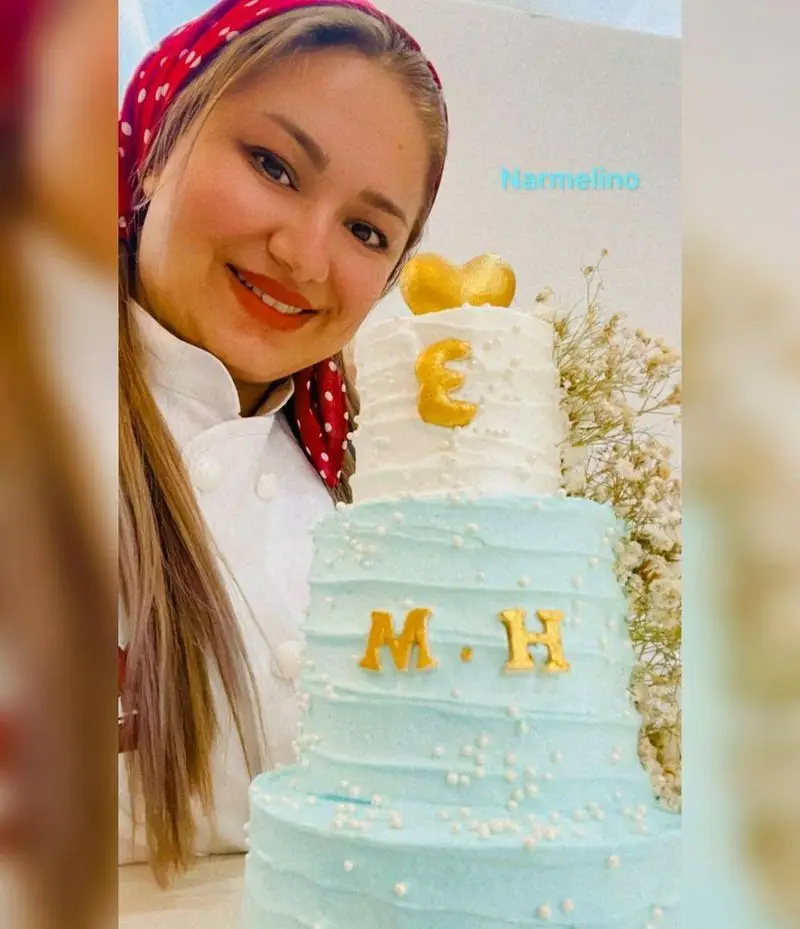 شیرینی‌پز قنادی نارملینو با کیک سه طبقه آبی و سفید زیبا، تزئین شده با حروف E و M.H، مناسب جشن تولد و مراسم خاص.
