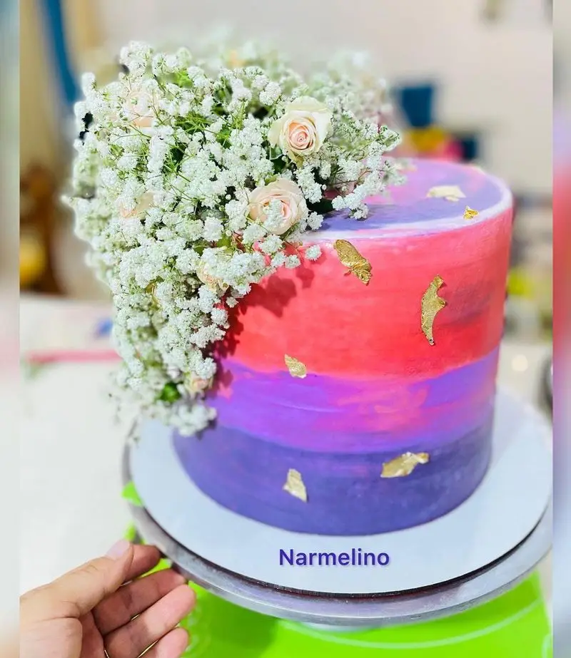 کیک آمبره شیک قنادی نارملینو با رنگ‌های جذاب صورتی و بنفش، تزیین گل رز طبیعی، گل عروس و ورق طلا.