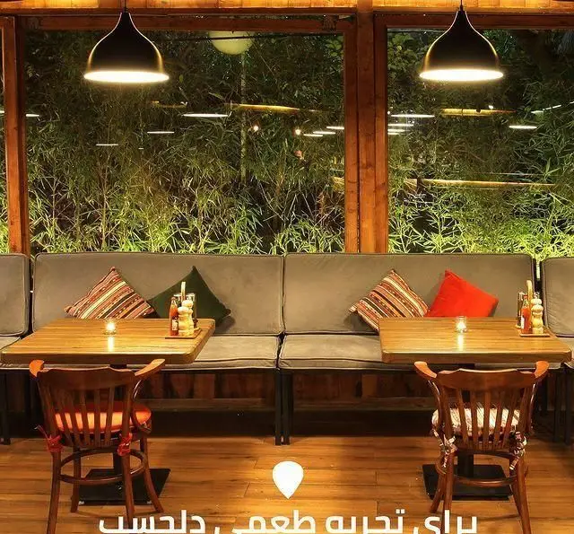 نمای داخلی جذاب کافه رستوران لوکال ولنجک با طراحی مدرن، میزهای چوبی، مبلمان خاکستری راحت و پنجره‌ای رو به فضای سبز بامبو