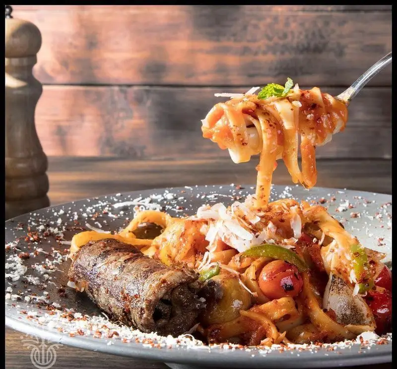 پاستا تالیاتل با سس گوجه، سبزیجات تازه و کباب لقمه رول شده سرو شده در کافه رستوران لوکال ولنجک. غذایی دلپذیر برای تجربه ای لذت‌بخش.