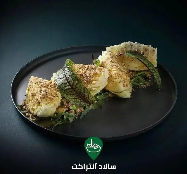 تصویر سالاد آنتراکت کافه رستوران لوکال ولنجک با برش‌های تازه کاهو، سس مخصوص و مغزهای خرد شده روی بشقاب مشکی.