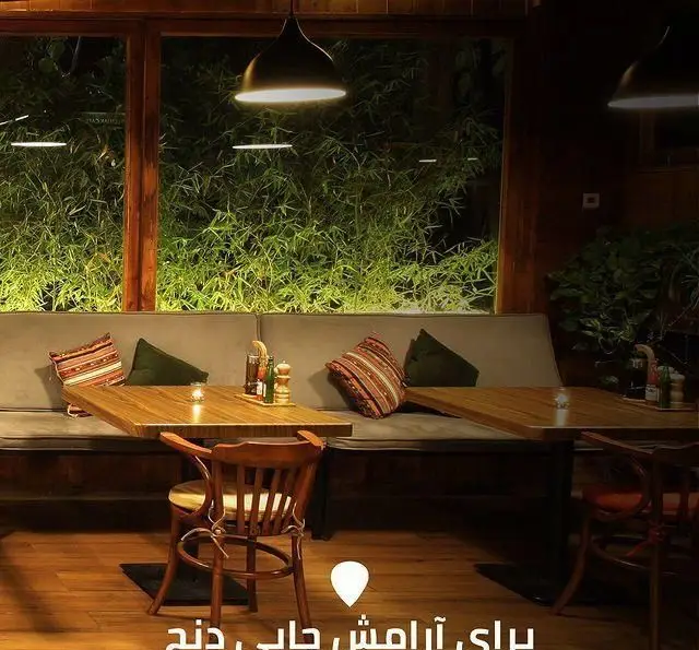 فضای دنج و آرام کافه رستوران لوکال ولنجک، با دکوراسیون چوبی دلنشین، نورپردازی گرم و چشم‌انداز زیبای سبز از پنجره.